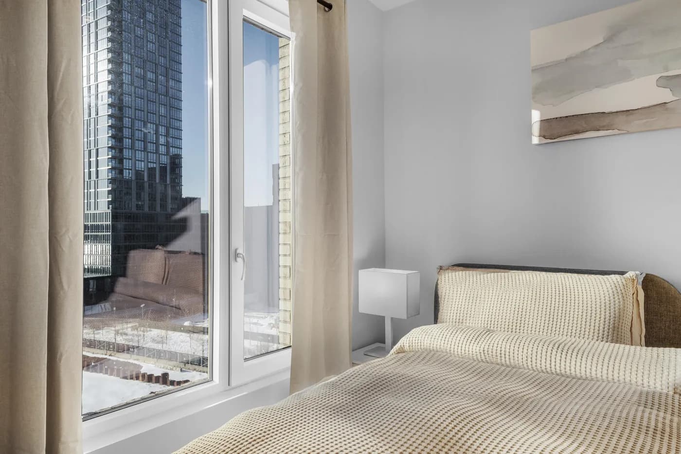 Furnished bedroom beside a floor-to-ceiling city window in Brooklyn