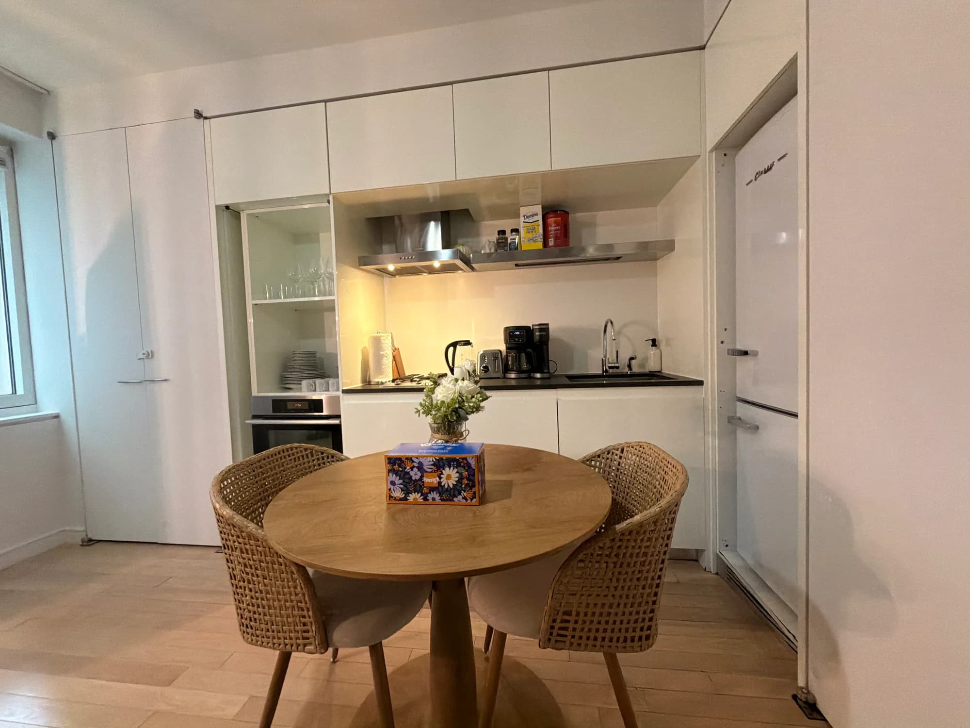 Round wood dining table and woven chairs in front of a white kitchen
