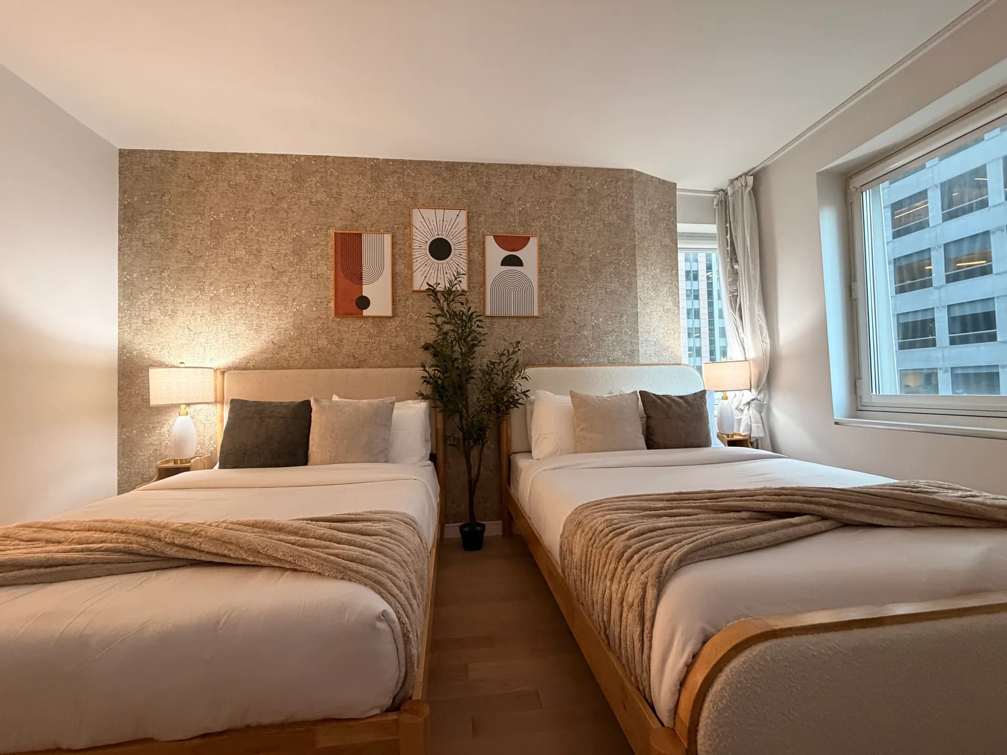 Two beds with warm bedside lamps beside a large window